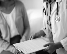 Black and white image of a doctor reading notes to a patient